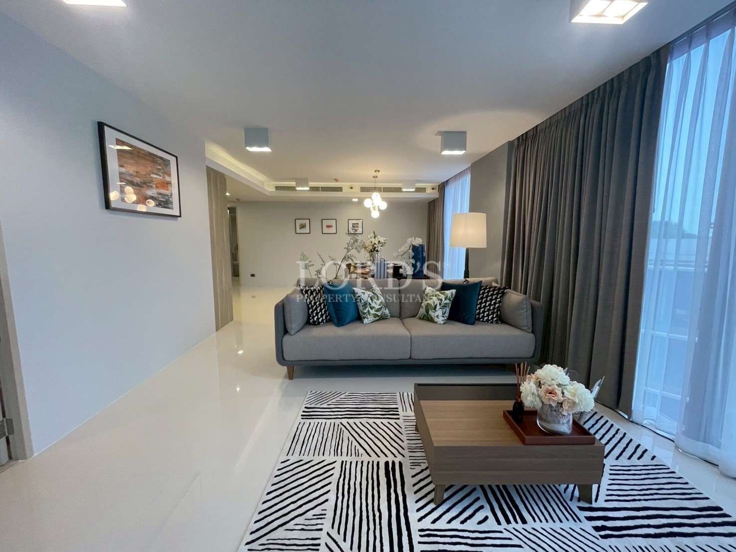 Modern living room with gray sofa, patterned rug, coffee table, and large window curtains.