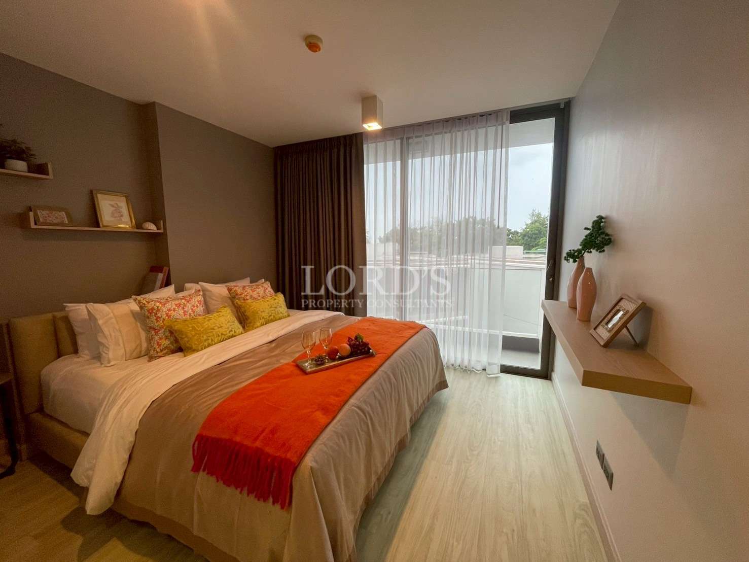 Cozy modern bedroom with a double bed, decorative pillows, soft lighting, and a balcony door with sheer curtains.