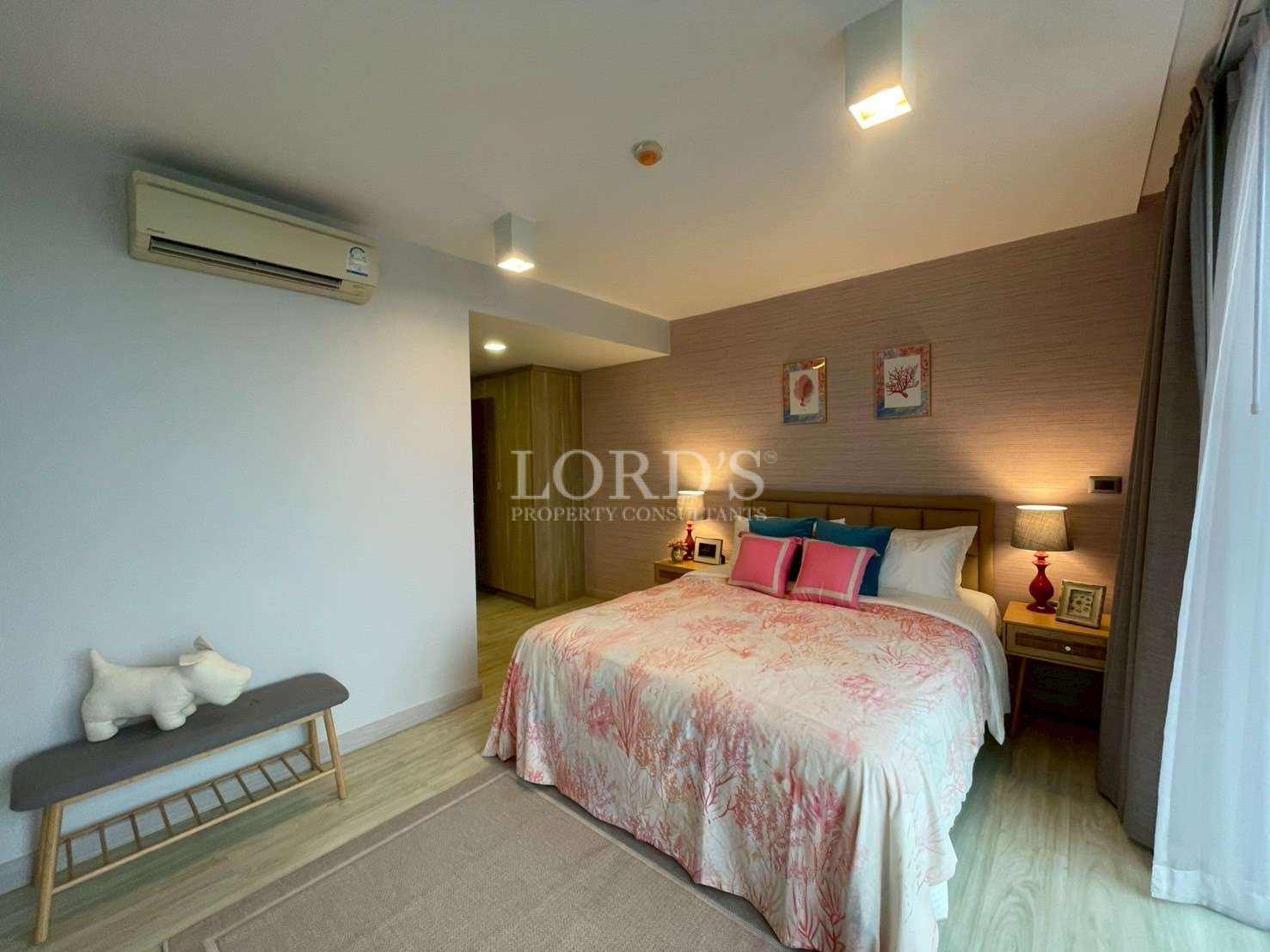 Modern bedroom with double bed, soft lighting, wall art, air conditioner, and wooden flooring.