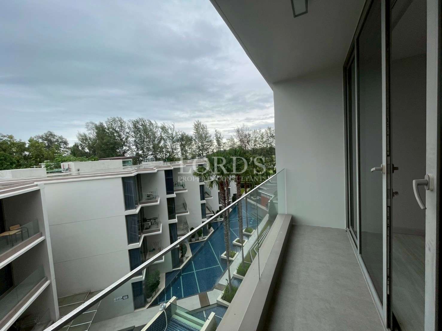 Private balcony overlooking a modern apartment complex with a swimming pool below.