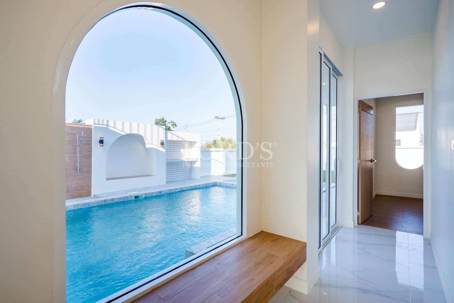 Arched indoor window overlooking private swimming pool with wooden seating ledge