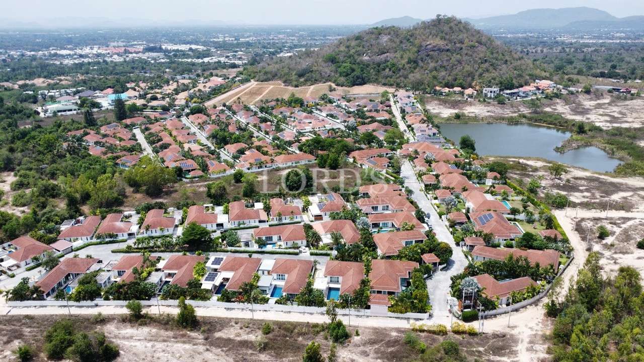 Aerial view of residential villa community with red-roof homes, green surroundings, and nearby hills
