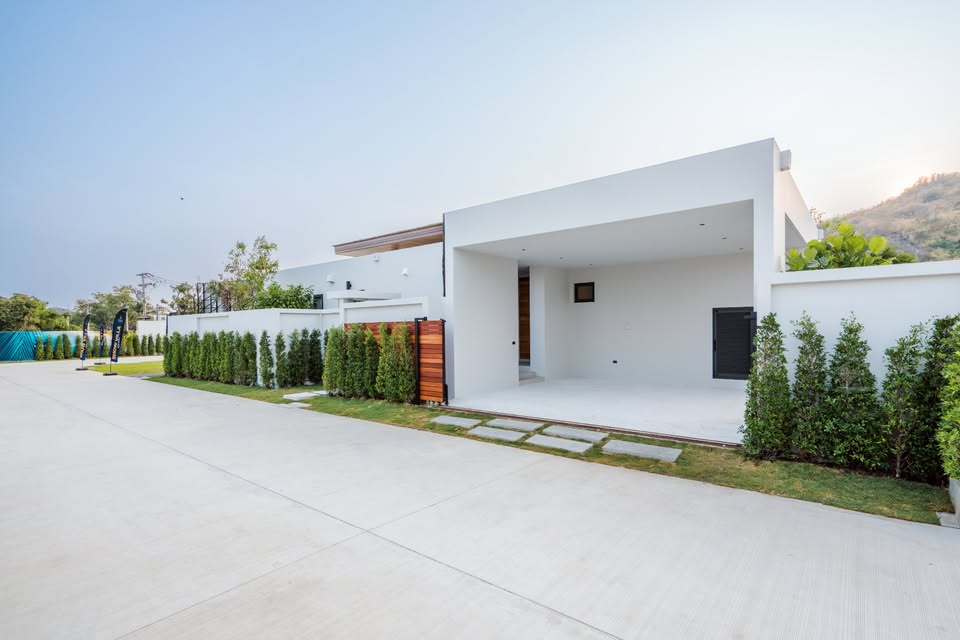 Modern luxury villa exterior with white minimalist design, covered parking, and landscaped greenery.