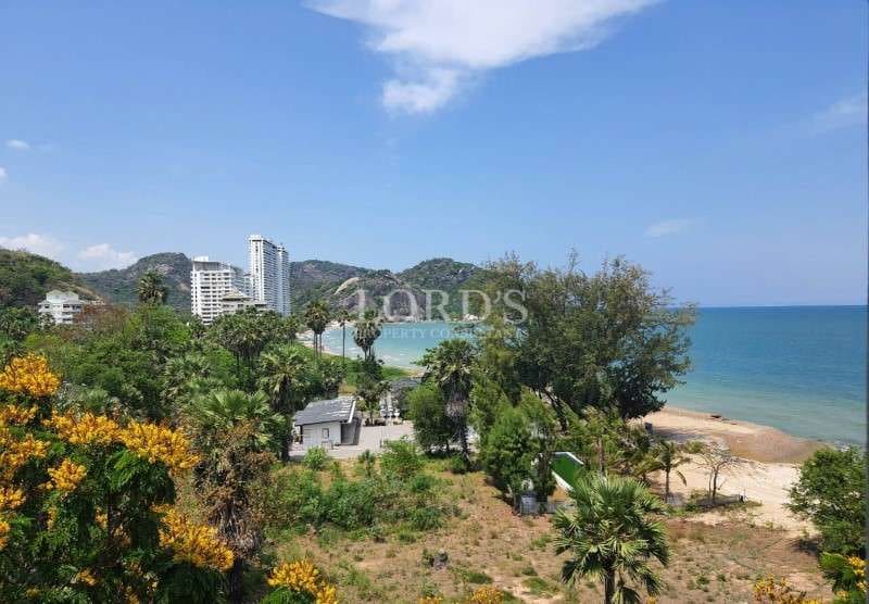 Coastal landscape with sandy beach, lush greenery, ocean view, and nearby residential buildings