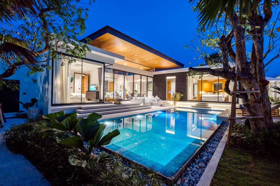 Luxury modern pool villa at night with private swimming pool, glass walls, and warm interior lighting.