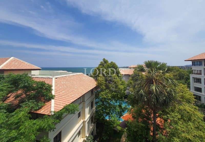 Resort-style residential buildings surrounded by lush greenery with ocean view in the background