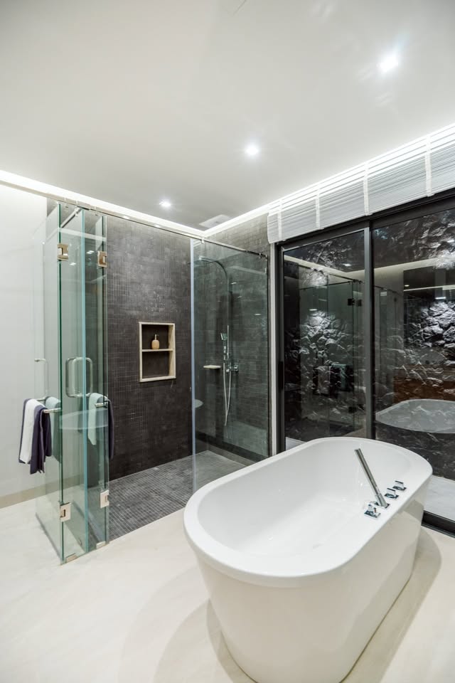 Modern luxury bathroom with freestanding bathtub, glass shower enclosure, and dark stone wall tiles.