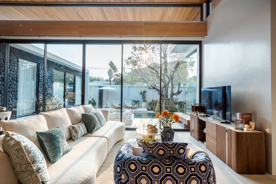 Luxury living room with modern sofa, wooden ceiling, TV console, and large glass doors opening to a private pool.