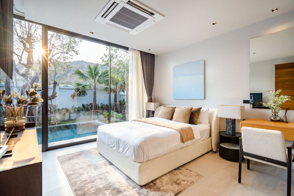 Modern luxury bedroom with pool view, soft neutral décor, large glass windows, and built-in work desk.