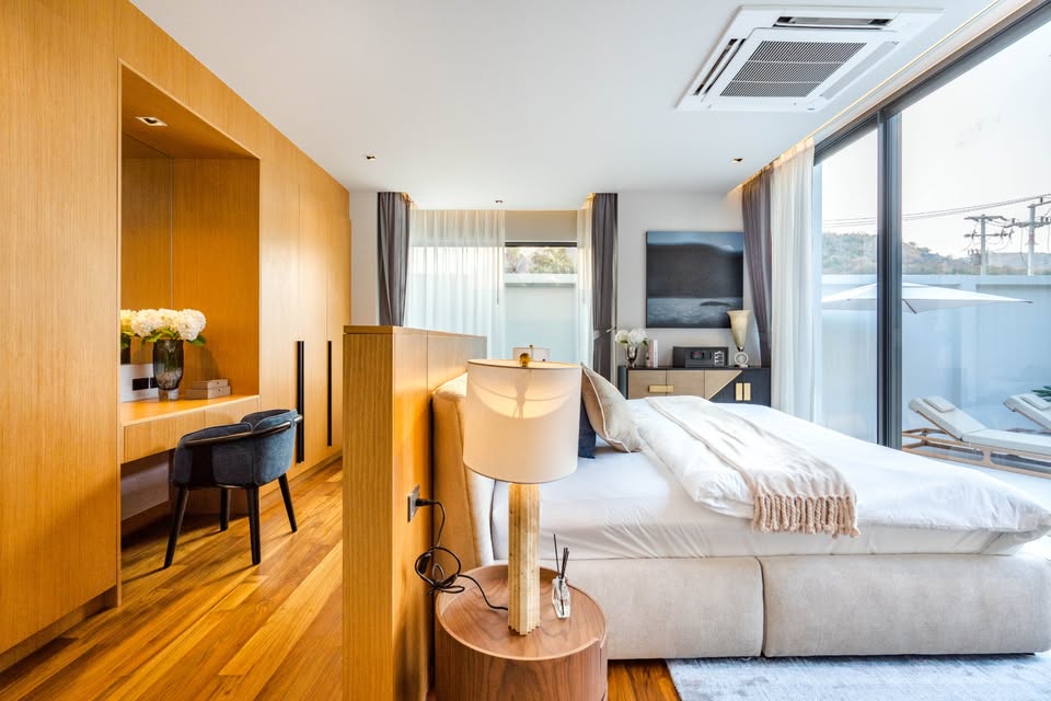 Modern luxury bedroom with wooden flooring, work desk, king-size bed, and large glass sliding doors.