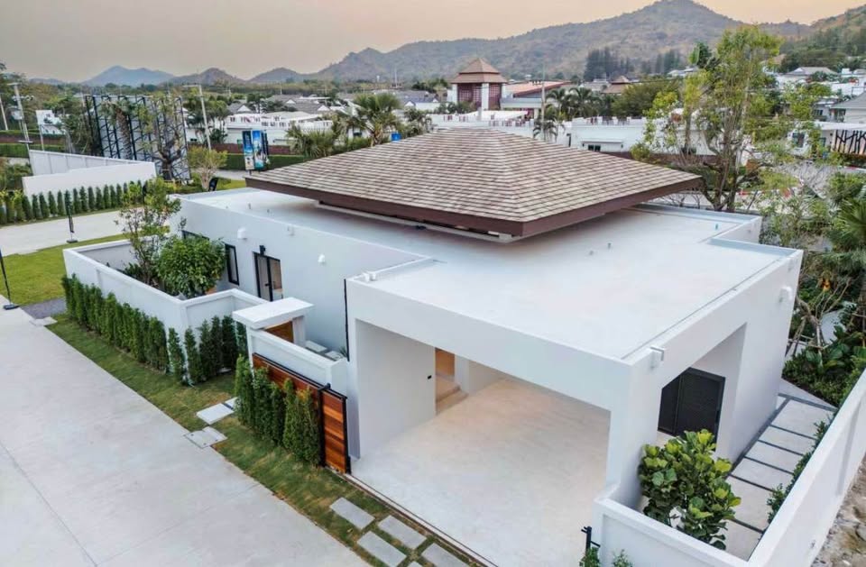 Modern luxury villa exterior with flat roof, covered parking, and landscaped garden in a residential area.