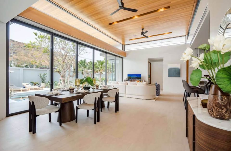 Modern dining and living area with wooden ceiling, large glass windows, and open-plan luxury interior.