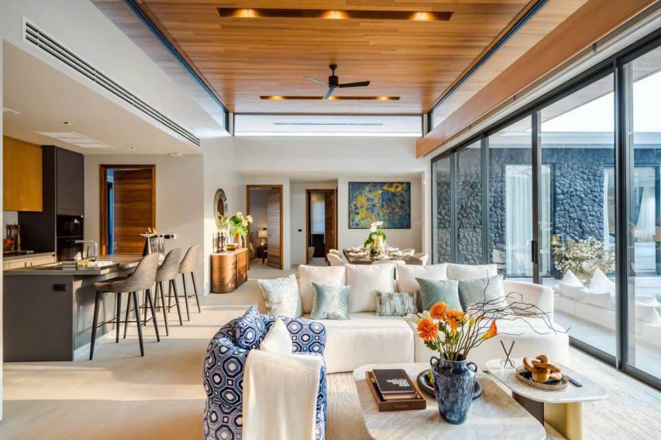 Luxury open-plan living room with modern sofa, kitchen island, wooden ceiling, and large glass sliding doors.