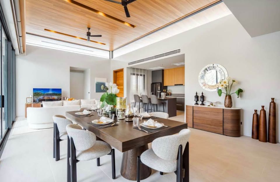 Modern open-plan dining and living area with wooden ceiling, large dining table, and minimalist decor.