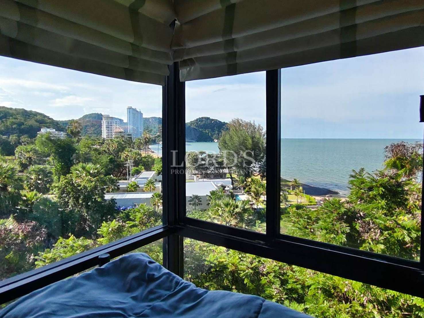 Ocean-view bedroom window overlooking lush greenery, coastal skyline, and blue sea