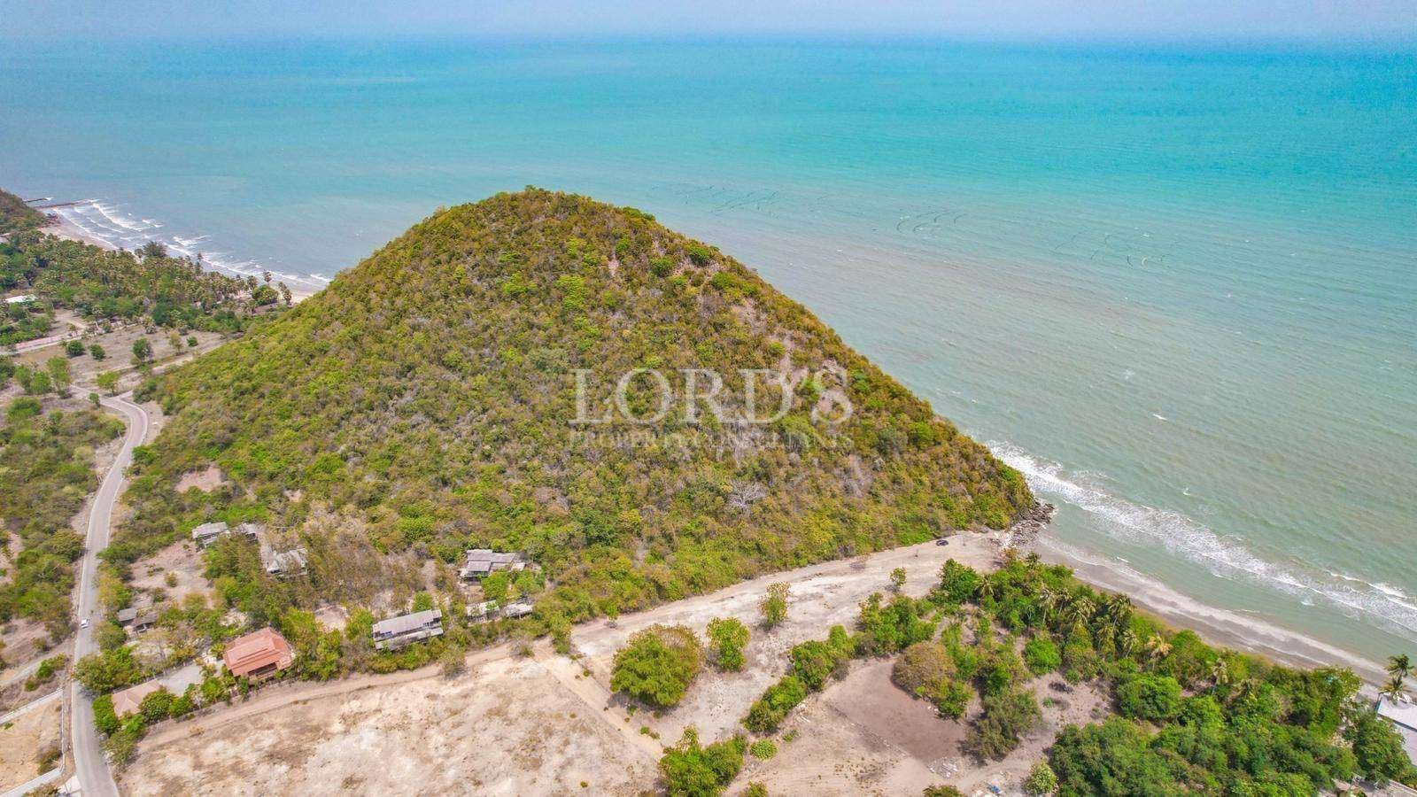 Aerial view of a green coastal hill surrounded by turquoise sea and a quiet shoreline.