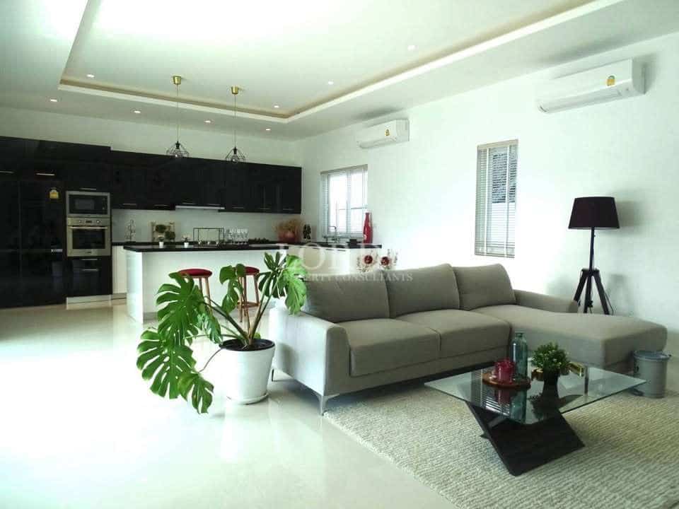 Modern open-plan living room with sofa, indoor plants, glass coffee table, and kitchen island