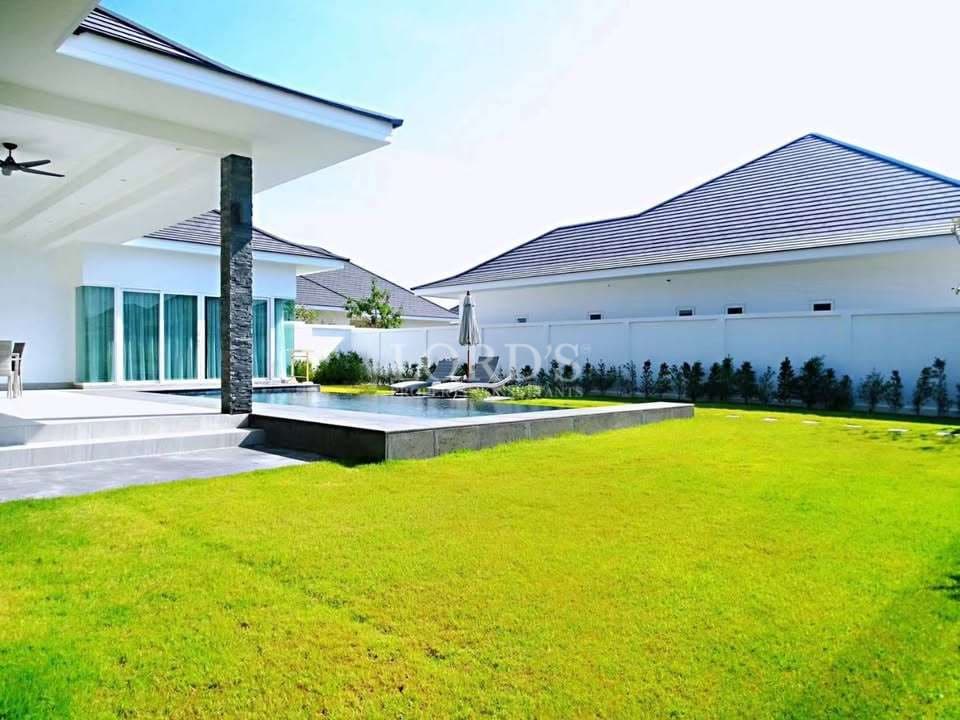 Modern villa exterior with green lawn, covered patio, and private pool area