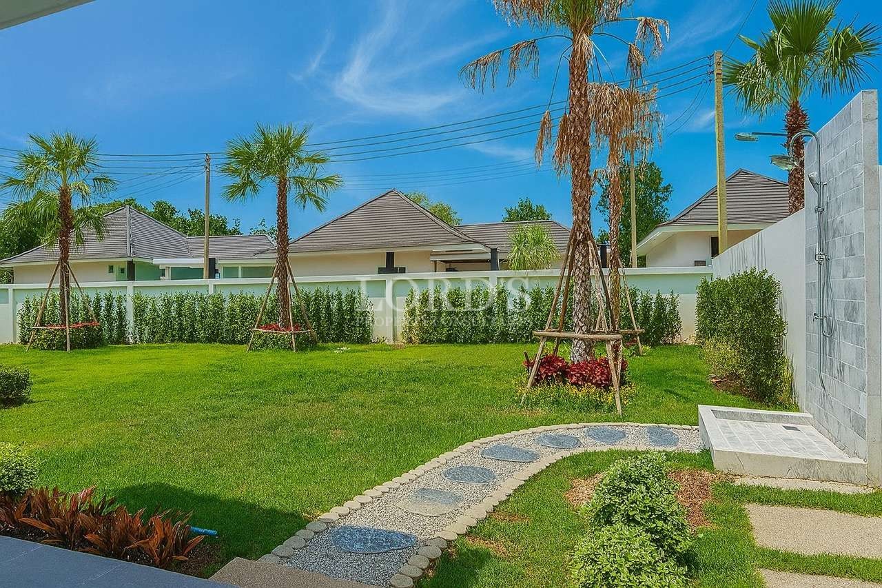 Landscaped garden with green lawn, palm trees, and stone pathway in a modern villa
