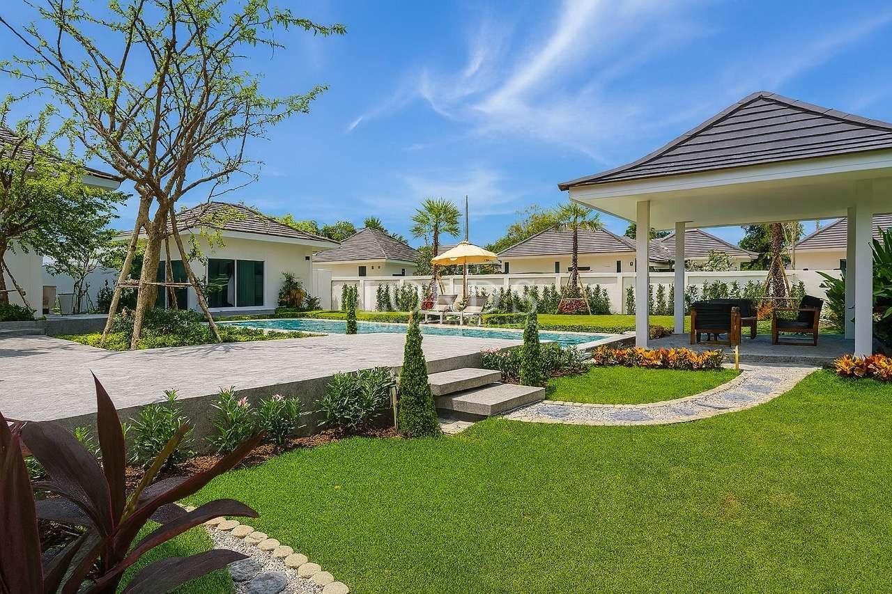 Luxury villa garden with swimming pool, landscaped lawn, and covered outdoor seating area.