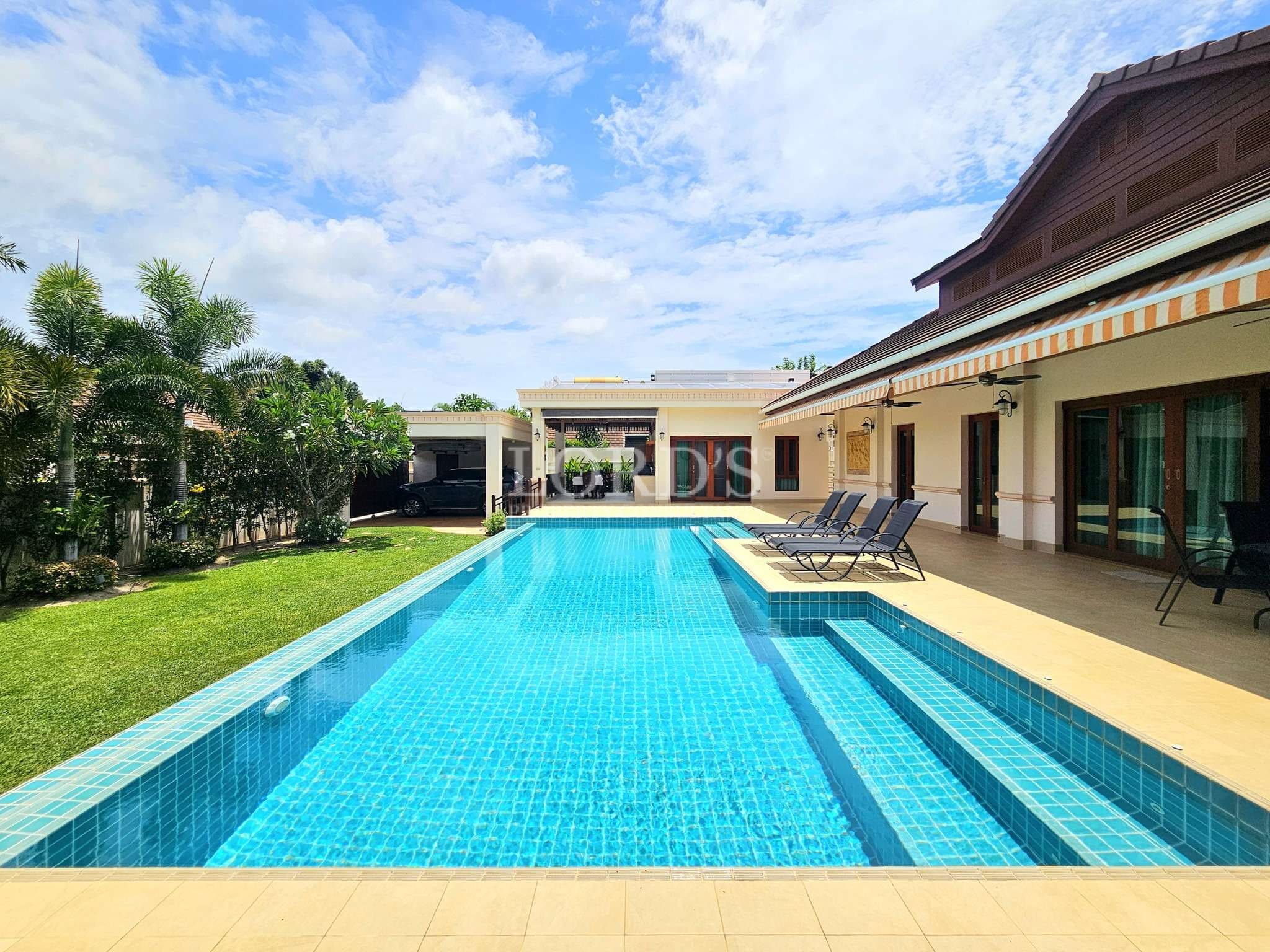 Private swimming pool with sun loungers beside a luxury villa and garden