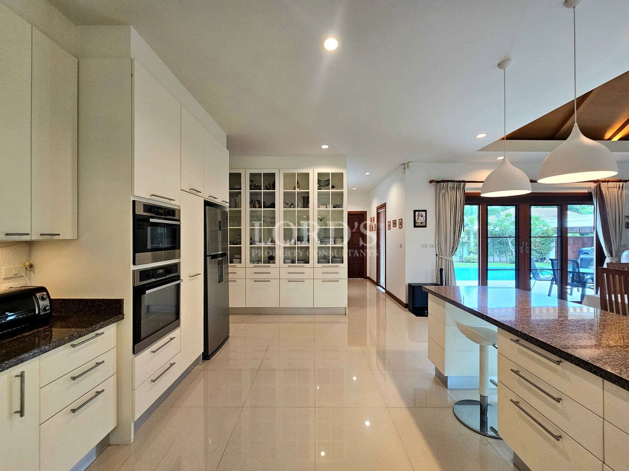 Modern open-plan kitchen with white cabinets, island seating, and pool view