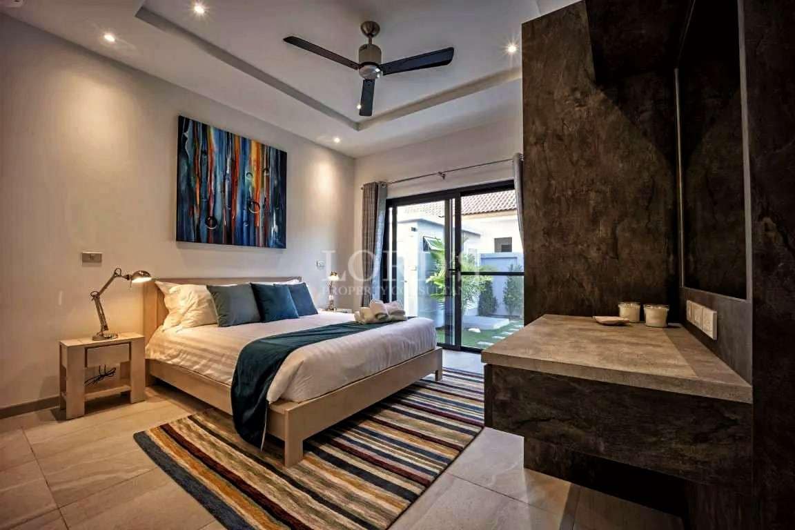 Modern bedroom with king-size bed, ceiling fan, stone accent wall, and garden-facing sliding glass doors