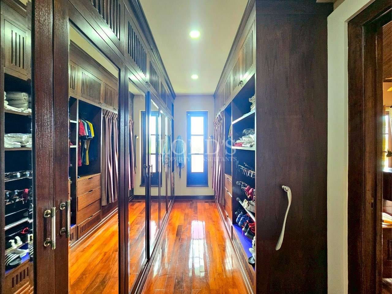 Luxury walk-in wardrobe with built-in wooden cabinets, mirrored doors, organized shelves, and hardwood flooring
