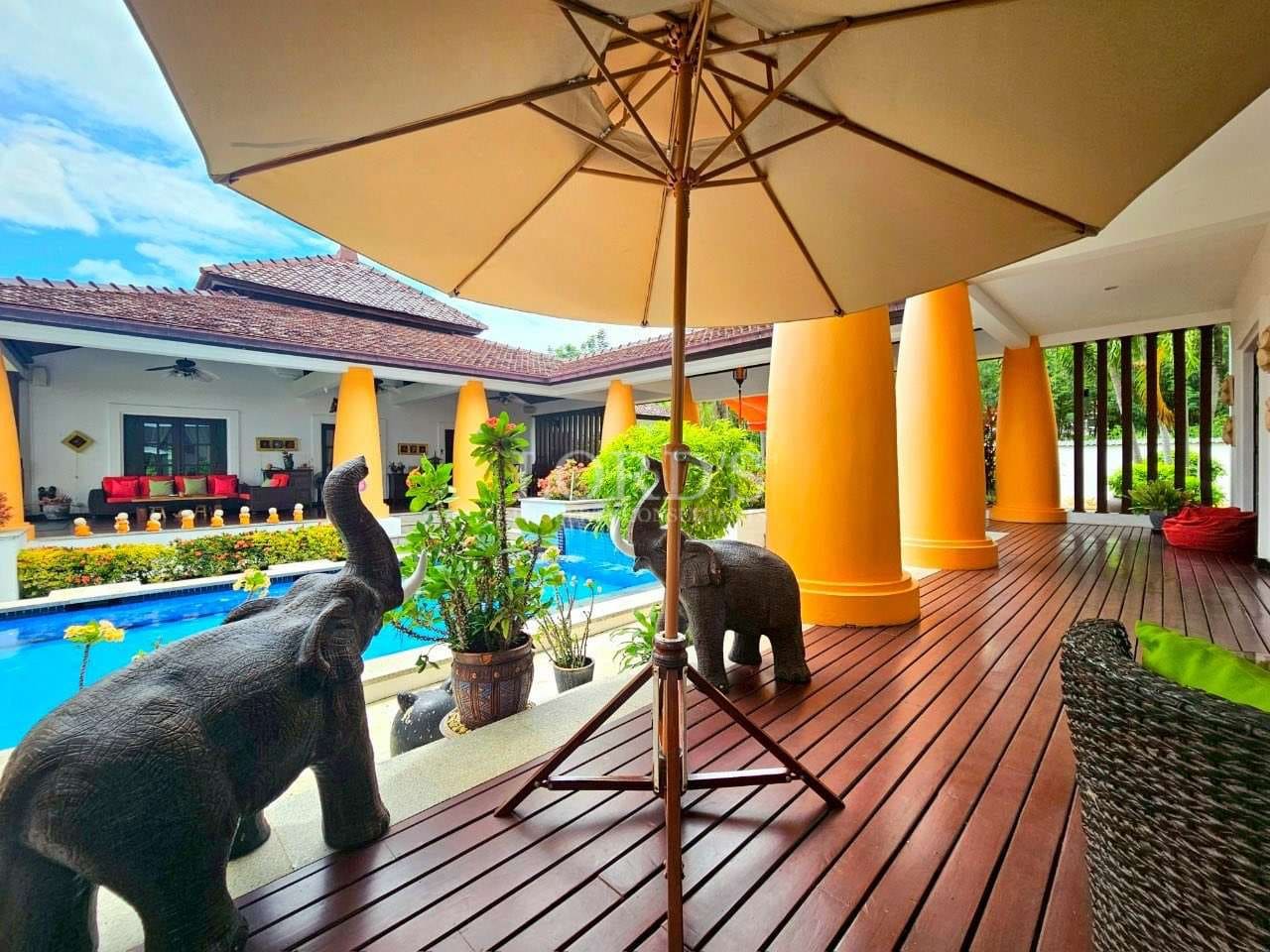 Luxury villa outdoor deck with swimming pool, elephant statues, wooden flooring, and large patio umbrella