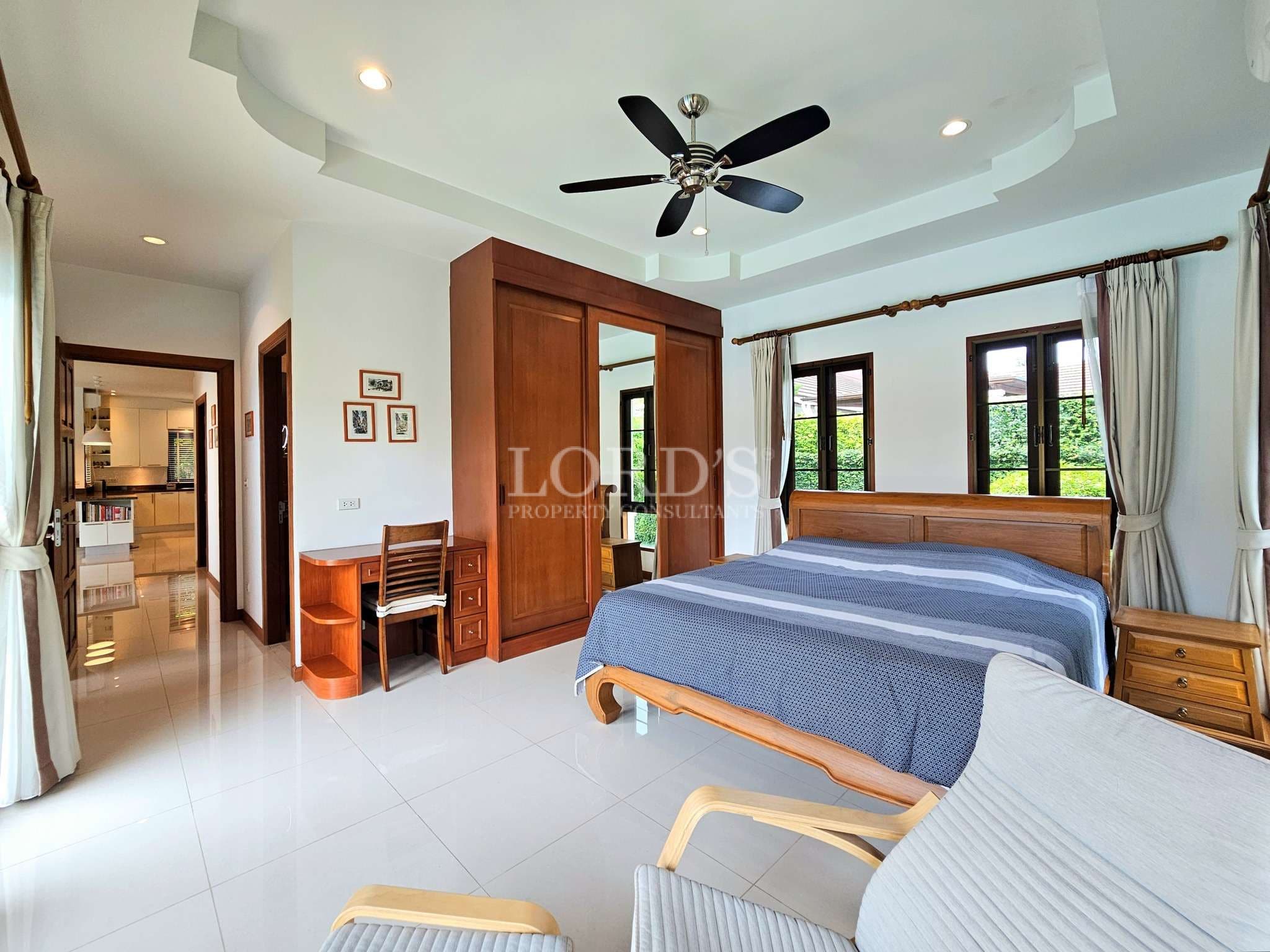 Spacious master bedroom with wooden bed, wardrobe, ceiling fan, and large windows