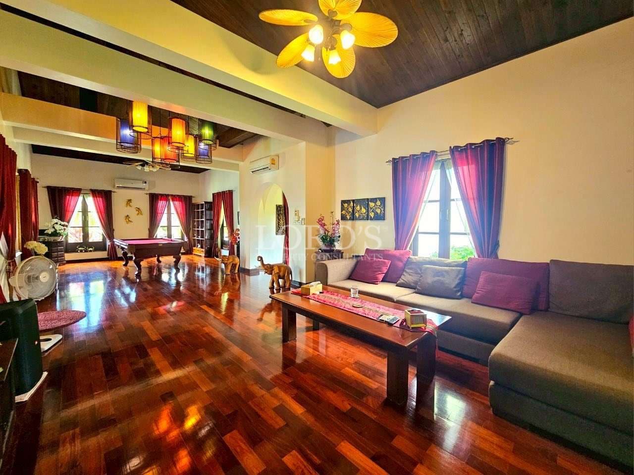 Spacious luxury living room with wooden floors, sectional sofa, pool table, and warm ambient lighting