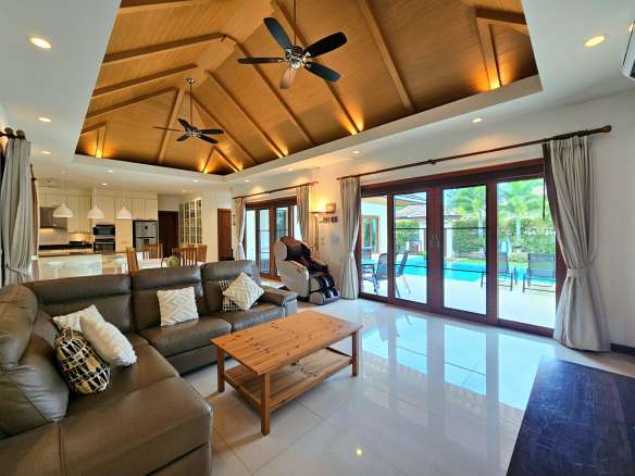 Luxury open-plan living room with high wooden ceiling, ceiling fans, and pool access