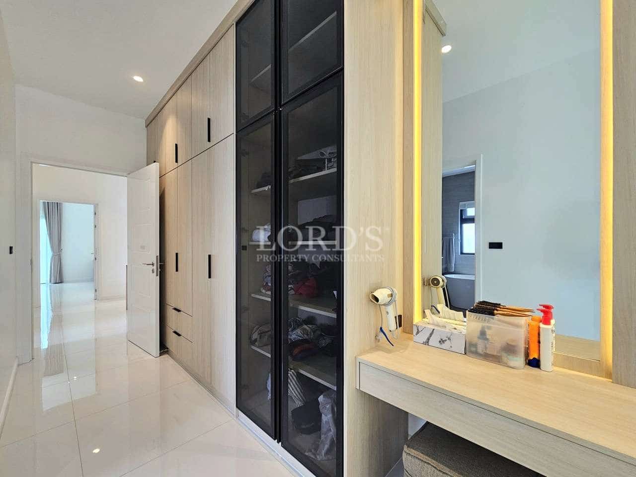 Modern walk-in wardrobe with built-in storage cabinets, glass doors, and vanity area