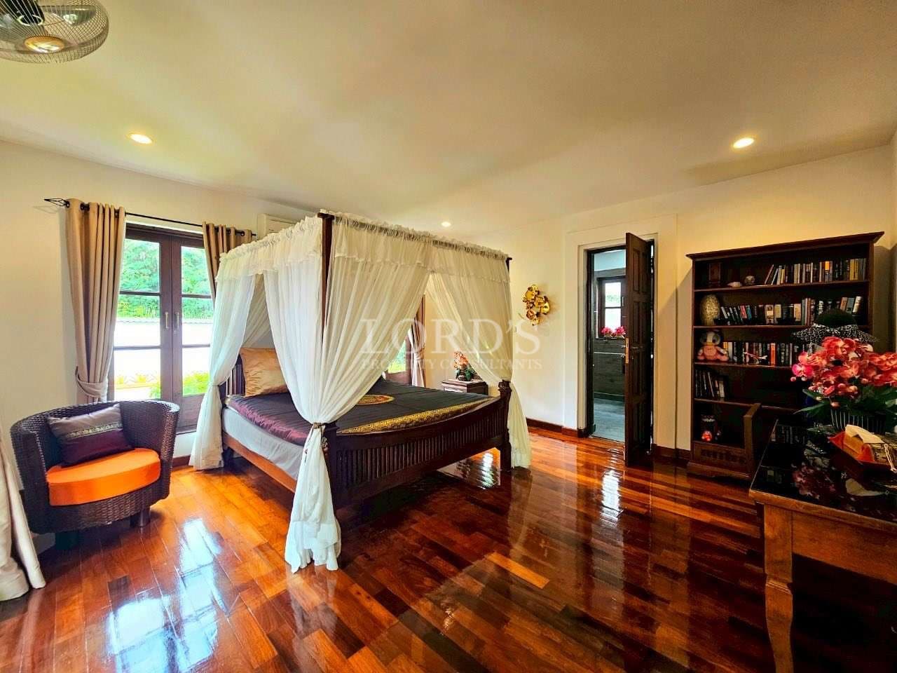 Luxury bedroom with four-poster canopy bed, sheer white curtains, polished wooden floor, and natural light
