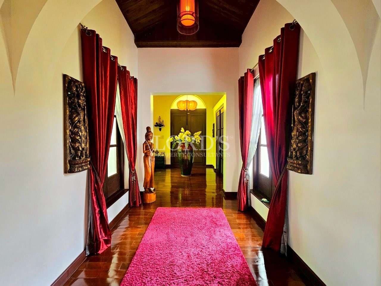 Elegant interior hallway with red curtains, polished wooden floor, and decorative statues under warm lighting