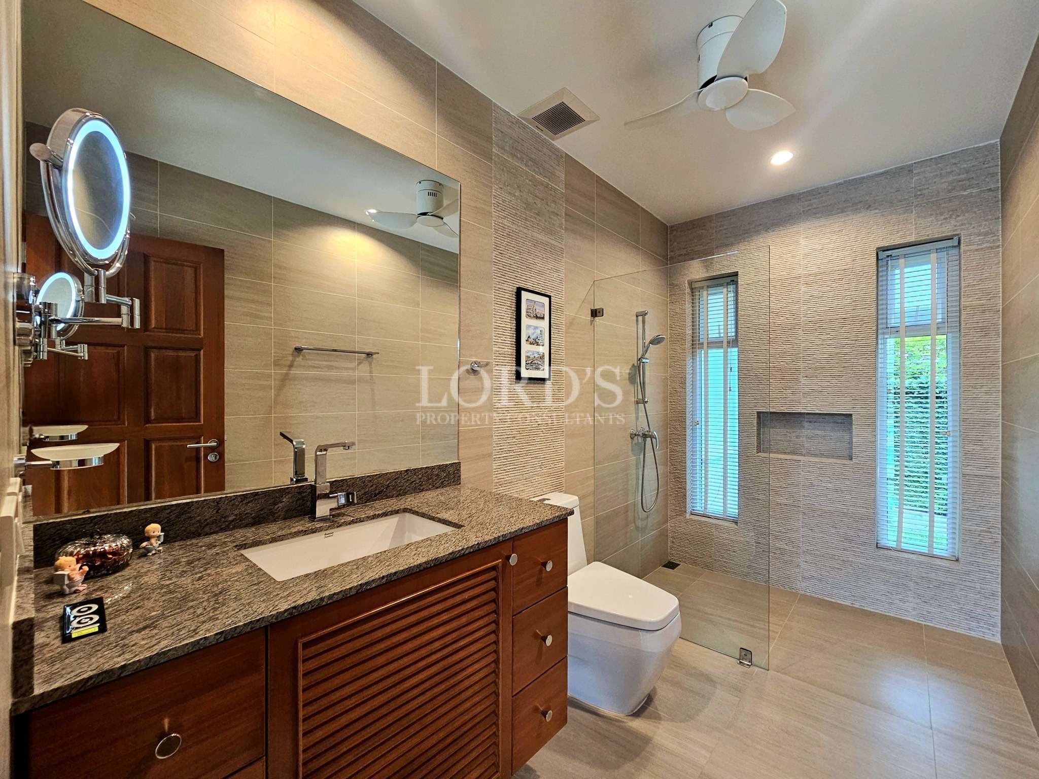 Modern villa bathroom with walk-in glass shower, granite vanity, and ceiling fan