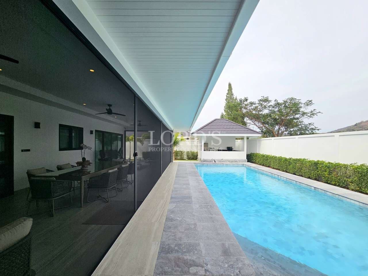 Private swimming pool alongside modern villa with covered terrace and glass walls