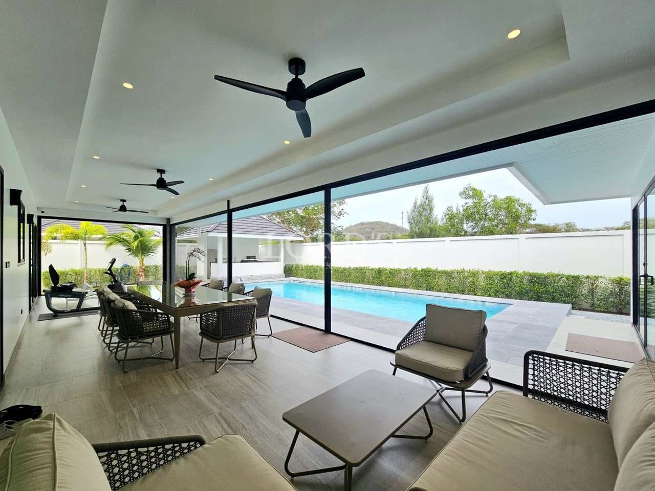Covered outdoor living area with seating, dining table, ceiling fans, and private swimming pool