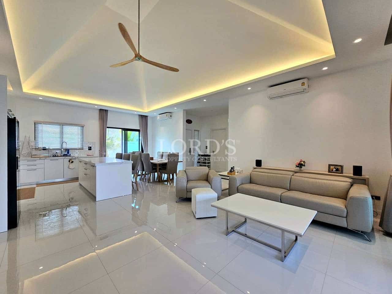 Open-plan living area with modern sofa, kitchen island, dining space, and recessed ceiling lighting
