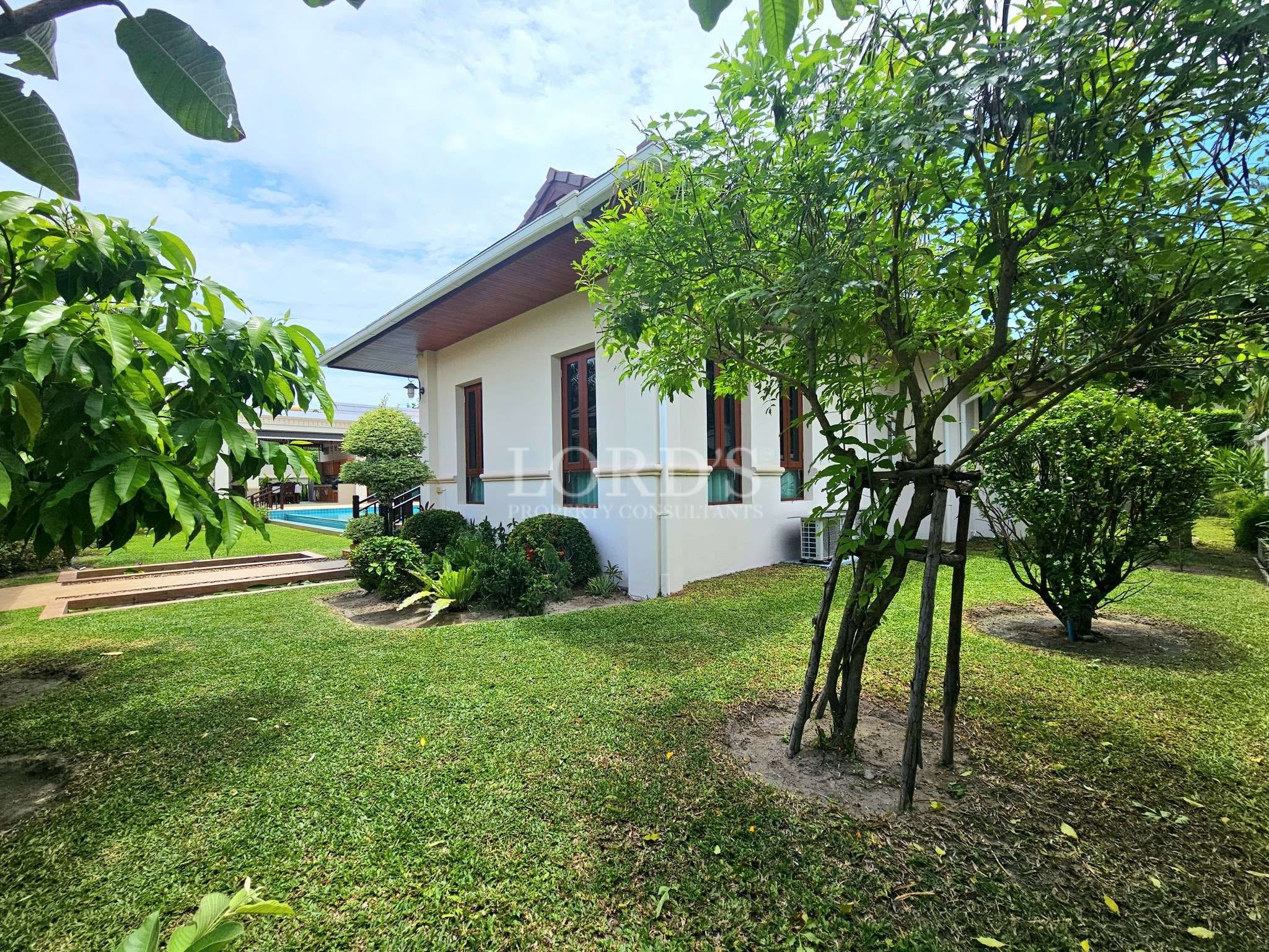 Modern villa exterior surrounded by green garden, trees, and lawn area