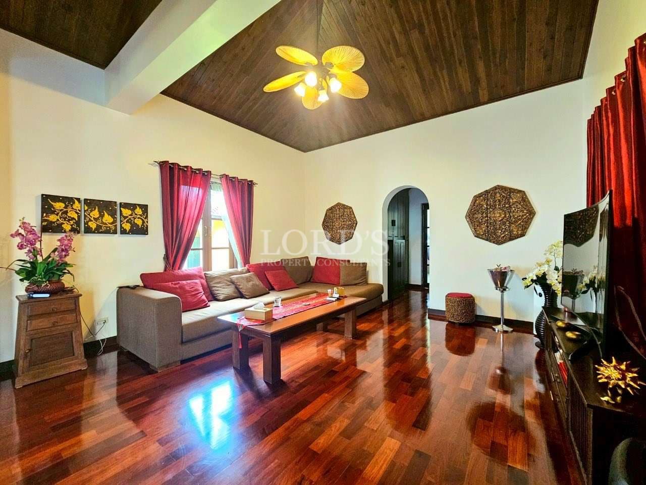 Elegant living room with wooden flooring, high wooden ceiling, modern sofa, and warm ambient lighting.