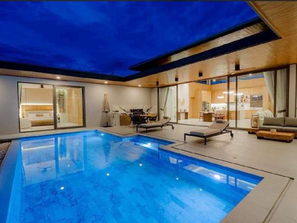 Luxury modern villa at night with illuminated private swimming pool and outdoor seating area.