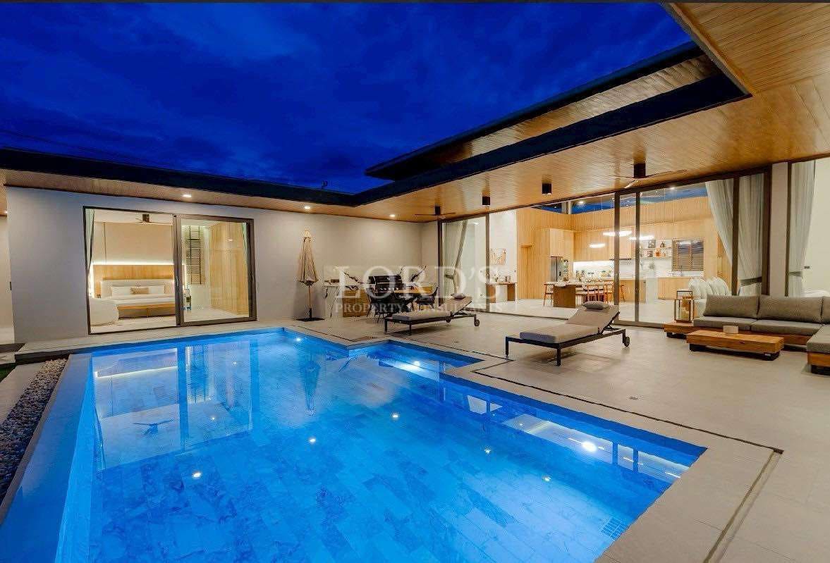 Luxury modern villa at night with illuminated private swimming pool and outdoor seating area.