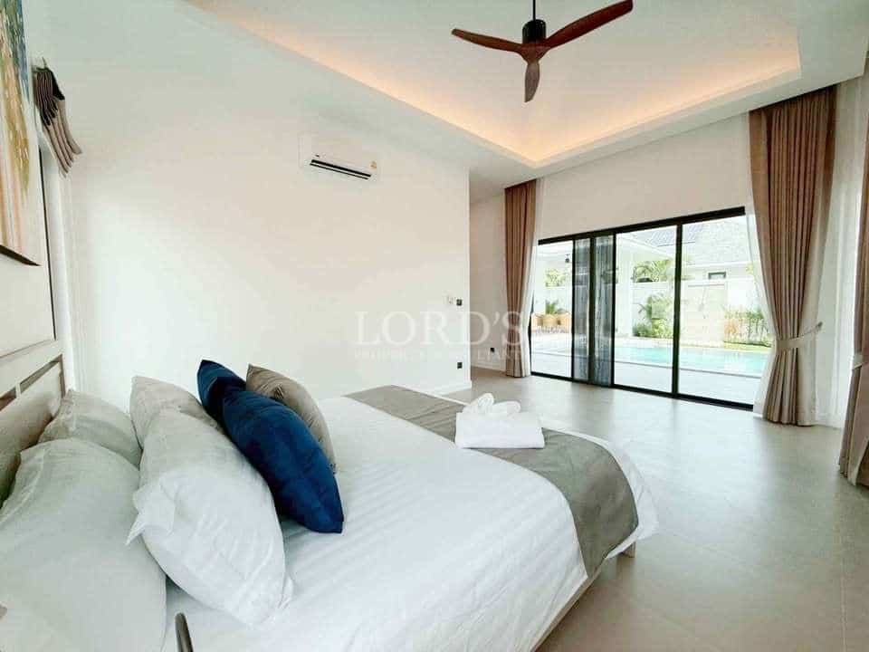 Modern bedroom with king-size bed, ceiling fan, and sliding glass doors opening to a pool view.
