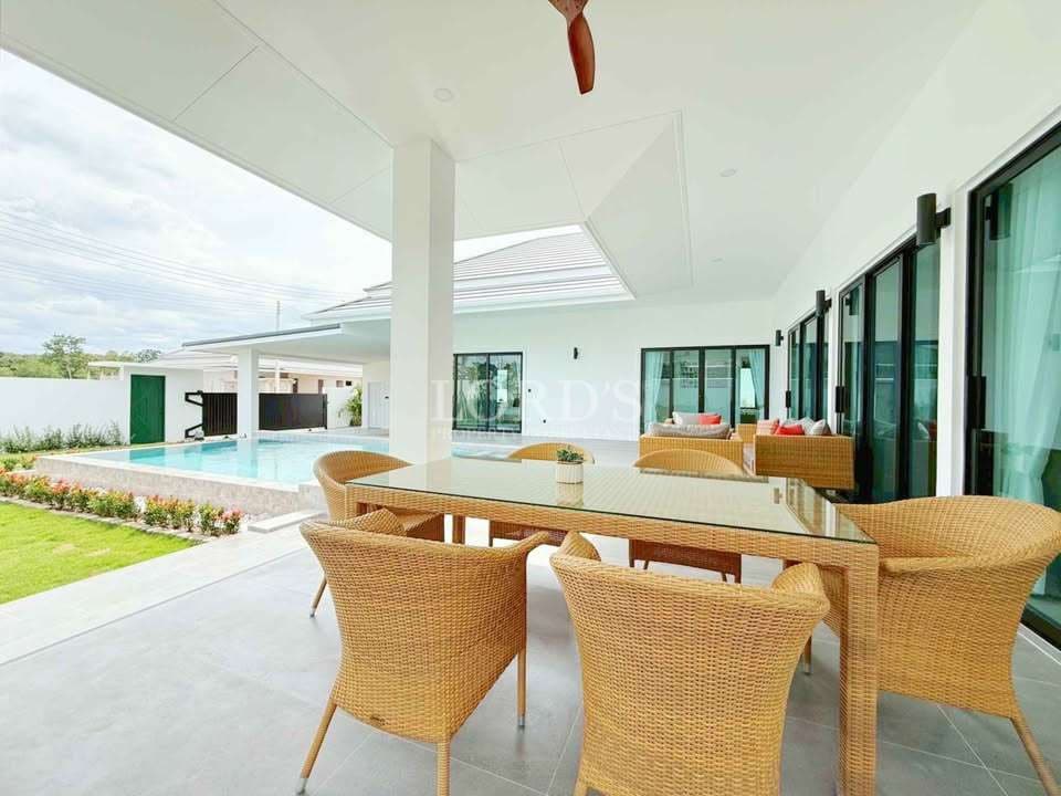 Luxury villa outdoor dining area with rattan furniture, covered patio, and swimming pool view.