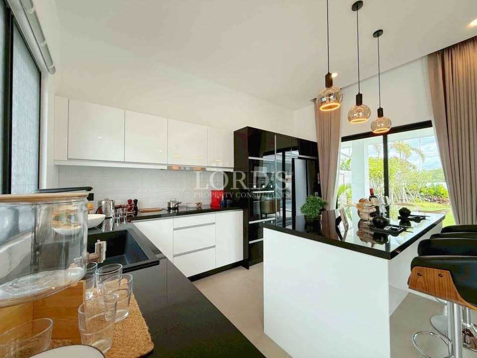 Modern white kitchen with black countertops, island seating, pendant lights, and large window views.