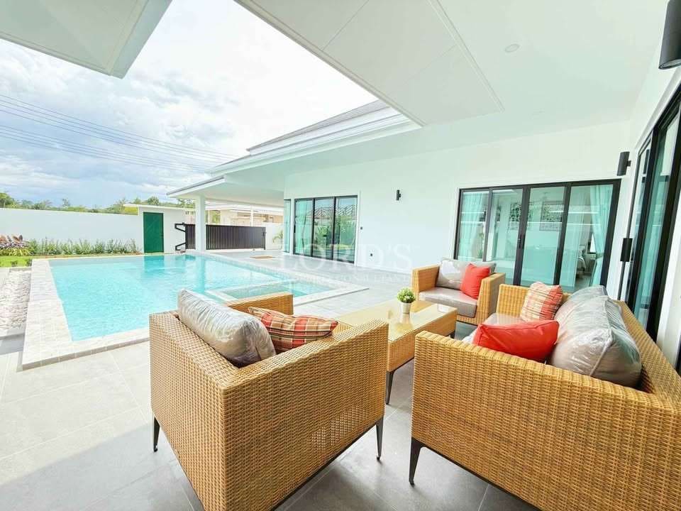 Luxury villa outdoor seating area with rattan furniture, swimming pool, and modern white architecture.