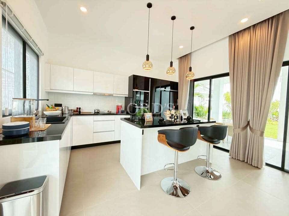 Modern white kitchen with black island countertop, pendant lighting, bar stools, and large glass windows.