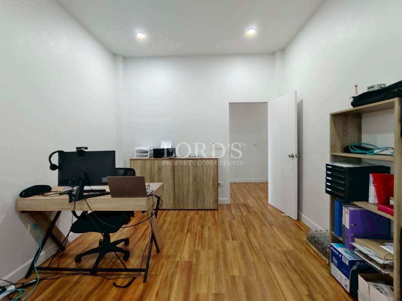 Modern home office room with wooden flooring, minimalist desk setup, storage shelves, and recessed ceiling lights