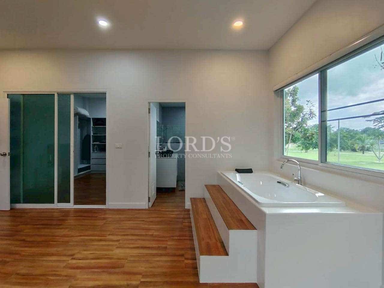 Bedroom with indoor bathtub, wooden floors, and large window overlooking garden.